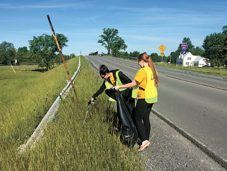 Thermo Fisher volunteer Ashley McRae reaches to pick more debris as co-worker Julia Doll holds open a garbage bag. Volunteers collected more than 19 bags of garbage June 10. (Photo by Chad Cowell/Thermo Fisher)